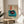 May include: Framed poster featuring a vintage turquoise turntable with black vinyl record and red center label, displayed on a round wooden side table next to a beige upholstered chair. The artwork has Japanese text in a red rectangular banner and cream background with additional text elements. Natural lighting creates soft shadows across the scene with a potted plant visible in the corner.