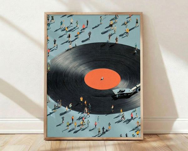 May include: Framed art print leaning against white wall on light wood floor. The poster shows an aerial view of a giant black vinyl record with orange label surrounded by tiny people casting long shadows on pale blue ground. A realistic turntable arm sits on the record's edge. The artwork has a surreal, miniature photography style in a thin light wood frame.