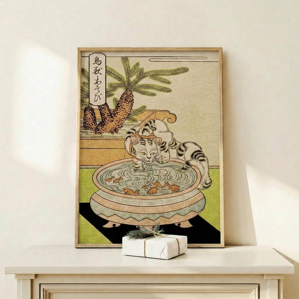 May include: Japanese woodblock print artwork in wooden frame showing striped cat drinking from decorative water basin with goldfish, pineapples visible in background, displayed on light wood shelf next to small white wrapped gift against cream wall