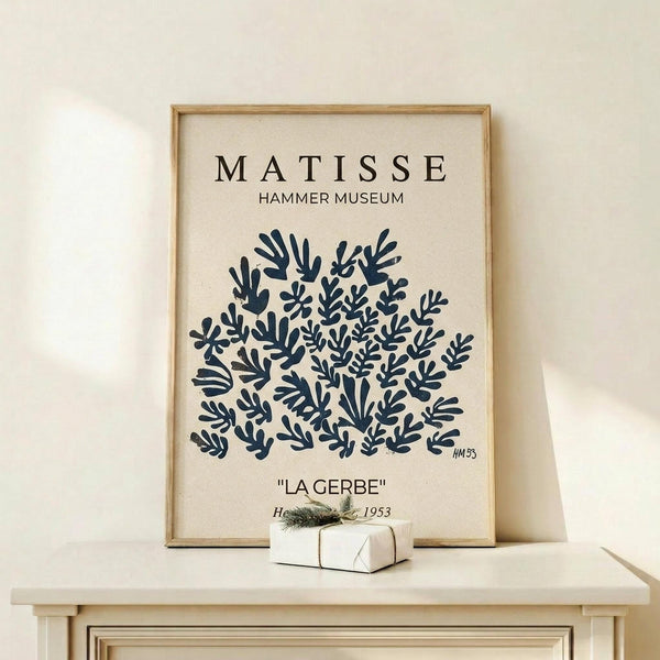 May include: Framed art print displaying Henri Matisse's La Gerbe artwork featuring navy blue abstract coral-like shapes on cream background, styled on light wood shelf with small wrapped gift box, against neutral wall