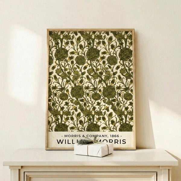 May include: Framed botanical poster with olive green floral pattern on cream background displayed on light wood console table. The vintage-style print features repeating ornate flowers and leaves in an intricate Arts and Crafts design. A small white gift box with natural twine and greenery sprig sits beside the wooden-framed artwork against a neutral wall.