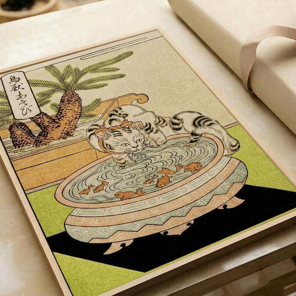 May include: Japanese woodblock print artwork displayed in an open book or portfolio, showing a striped cat bathing in a decorative ceramic basin with small fish swimming around it. A pineapple plant sits in the background. The print features traditional ukiyo-e style with muted earth tones, green accents, and Japanese text in the upper left corner. The book rests on a light wooden surface with neutral fabric visible in the background.