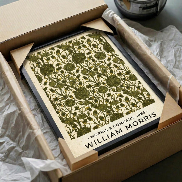 May include: Vintage botanical poster with intricate green floral pattern featuring detailed leaves, vines, and circular flower motifs on cream background. Black-framed print sits in open cardboard shipping box with white tissue paper and wooden tube packaging materials visible around it on neutral surface.