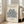 May include: Framed poster with cream background featuring dark blue botanical cut-out shapes resembling coral or seaweed, displayed leaning against white wall next to beige upholstered chair in bright room with large windows and wooden floors.