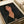 Portrait of a woman with dark hair and elongated neck in Modigliani's distinctive style, featuring warm peachy skin tones against a dark background with a small pink rose detail. The artwork is displayed as a print in an open art book or portfolio with cream-colored pages and white ribbon visible at the edges.