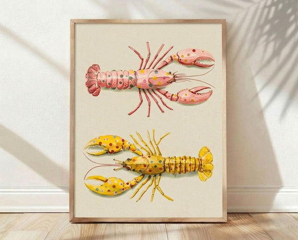 May include: Framed art print displaying two whimsical lobsters with colorful polka dot patterns in pink and yellow tones, shown in thin wooden frame leaning against white textured wall on light wooden floor with soft natural lighting and plant shadows