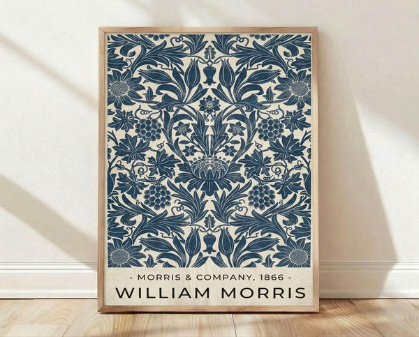 May include: Framed vintage botanical poster with intricate navy blue floral pattern on cream background, featuring symmetrical design of leaves, grapes, and ornate flowers. Wooden frame sits on light hardwood floor against white wall with soft natural lighting creating subtle shadows.