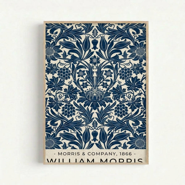 Ornate blue and cream botanical poster print featuring symmetrical floral damask pattern with sunflowers, grape clusters, and decorative leaves in William Morris Arts and Crafts style. The intricate design shows repeating motifs in deep navy blue against an off-white background, displayed in a simple light wood frame against a white wall.