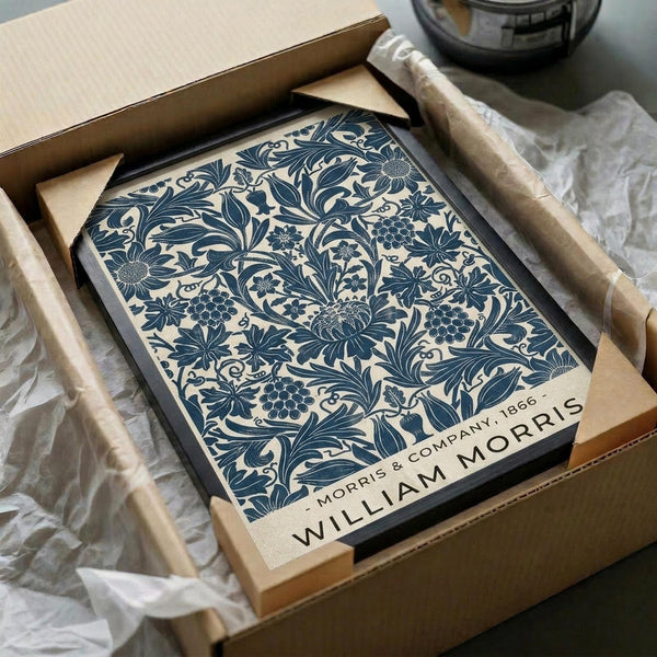May include: Vintage William Morris botanical poster print with intricate blue floral pattern on cream background, displayed in black frame inside opened cardboard shipping box with white tissue paper protection. The detailed design features intertwining vines, flowers, and foliage in classic Arts and Crafts style.