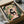 May include: Framed poster artwork being unpacked from a cardboard shipping box with protective wrapping. The illustration shows a black cat with bright yellow eyes sitting on pink tile flooring while reading a newspaper, surrounded by lush green houseplants including snake plants, pothos, and framed botanical art on a coral pink wall. The print has a cozy indoor garden aesthetic with warm, vibrant colors.