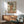 May include: Japanese woodblock print artwork showing a woman in elaborate orange and coral kimono holding a decorative fan, displayed in wooden frame above mid-century modern walnut credenza with ceramic table lamp, next to sage green upholstered armchair with wooden arms in sunlit room with white walls