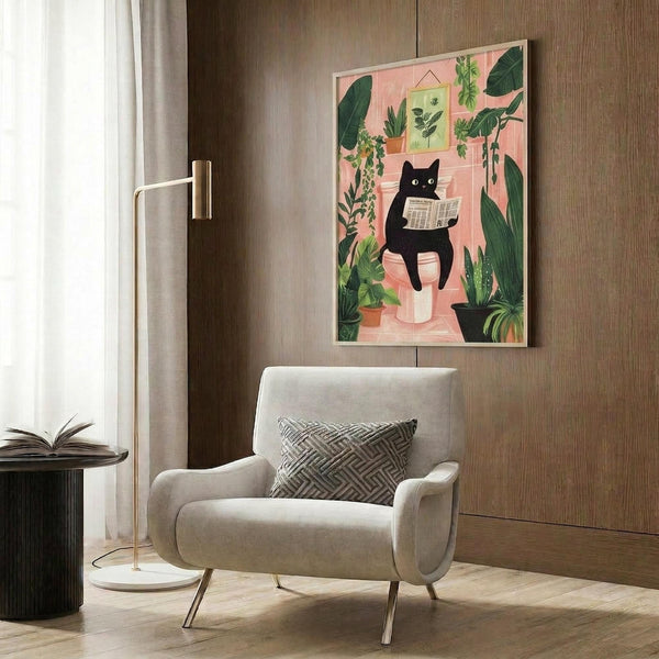 May include: Framed poster print mounted on wood-paneled wall above cream upholstered armchair with geometric pillow. Artwork features black cat reading newspaper surrounded by lush green plants on coral pink background. Modern reading nook with brass floor lamp, dark round side table with open book, and natural lighting from window with sheer curtains.