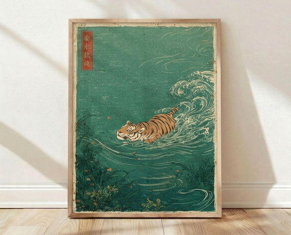 May include: Framed vintage Japanese woodblock print featuring an orange and black striped tiger swimming through turquoise-green churning waves. The ukiyo-e style artwork shows dynamic water swirls and splashes around the tiger, with dark vegetation at the bottom and a red text cartouche in the upper left corner. The print is displayed in a light wooden frame, leaning against a white wall on light wood flooring with natural shadows.