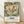 May include: Framed vintage botanical poster leaning against white wall on wooden floor. Features large cream peony flower with red accents and teal-green foliage in William Morris style. Black text below reads "Cotton Print Exhibition" with Underground logo and "South Kensington" location details. Natural wood frame, soft fabric shadows visible on textured white wall background.