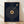 May include: A framed poster with navy blue background featuring song lyrics arranged in a spiral pattern around a golden vinyl record design. The text includes placeholders for song name, artist, and personal message at top, with "Oliver & Meaghan" at bottom. A golden turntable arm extends from upper right. Wood frame sits on light wooden floor against white wall with natural lighting creating soft shadows.