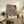 May include: Framed vintage botanical print with intricate floral pattern in navy blue, coral, and cream tones displayed on rustic wooden sideboard. Room scene shows fern plant, ceramic vase, stacked books, and brown leather chair arm. Artwork features ornate Victorian-style flowers and foliage in decorative wallpaper design against neutral wall.