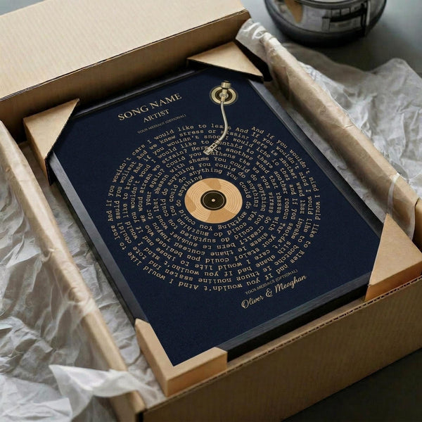 May include: Navy blue poster with golden vinyl record design and personalized song lyrics arranged in circular text pattern around the record. Framed artwork sits in wooden gift box with tissue paper, displayed next to decorative glass vessel on neutral surface. Elegant presentation suggests premium quality print with metallic accents.