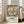 May include: Framed vintage botanical poster featuring large cream and coral flower with detailed petals surrounded by teal and green foliage. Text below reads "Cotton Print Exhibition" with London Underground logo and "South Kensington" station details. Light wood frame leaning against white wall next to beige upholstered chair in bright, naturally lit room with hardwood floors.