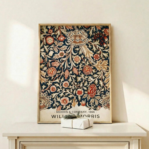 May include: Framed botanical poster with intricate floral pattern on navy background, featuring cream and coral flowers, ornate leaves, and decorative vines in William Morris style. Golden wood frame sits on light wooden shelf next to small white gift box with evergreen sprig. Cream colored wall backdrop creates minimalist display setting.