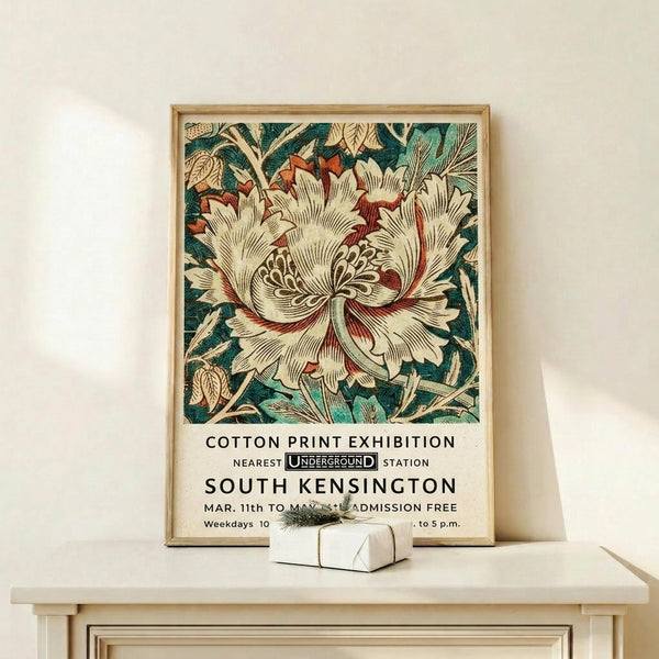 May include: Framed vintage botanical poster featuring large cream and coral peony flower with dark teal foliage, displayed on light wood console table beside white gift box. Exhibition-style poster shows William Morris-inspired floral design with Underground station reference and event details in black text below ornate bloom.