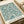 Vintage botanical poster print featuring intricate teal and cream willow branch pattern with flowing leaves and organic curves. The design displays William Morris & Company 1866 text at bottom right corner. Print appears on cream paper with visible texture, photographed alongside neutral packaging materials and cream ribbon on wooden surface.