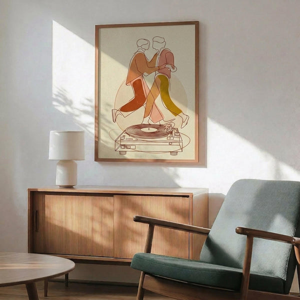 May include: Framed poster featuring two minimalist line-drawn figures dancing above a turntable, rendered in warm earth tones of orange, rust, and yellow against cream background. Displayed above mid-century wooden credenza with white ceramic lamp, next to sage green upholstered armchair with wooden arms. Bright natural sunlight creates dramatic shadows across white wall in modern living room setting.