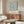 May include: Framed botanical poster with teal willow branch pattern on cream background, displayed above walnut credenza in minimalist living room with white curved chair, glass coffee table, and brass floor lamp
