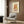 May include: Modern living room scene showing framed poster on wood paneled wall featuring two dancing figures in orange and yellow clothing above a vintage turntable, illustrated in minimalist line art style. Cream-colored armchair with geometric pillow, brass floor lamp, and dark round side table with open book complete the contemporary interior setting.