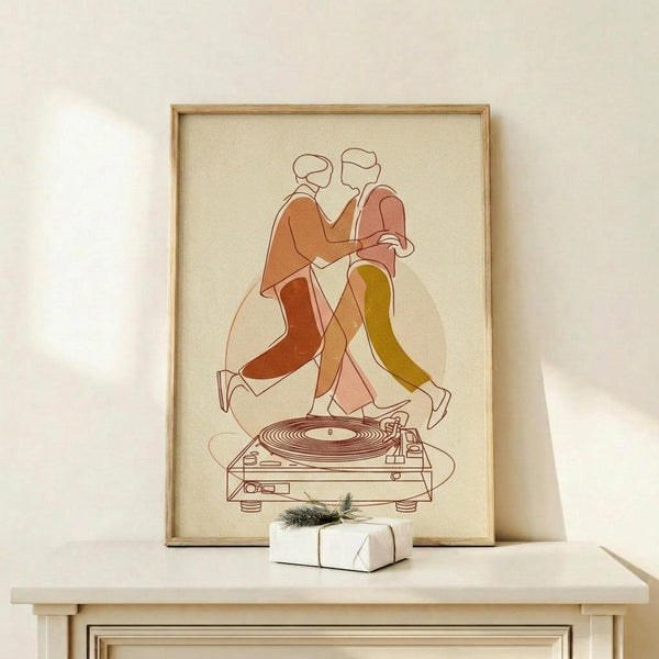 May include: Framed poster print showing two abstract figures dancing on top of a vinyl record player, rendered in warm earth tones of orange, rust, pink and olive green against a cream background. The minimalist line art depicts the couple in flowing clothing with simple outlined faces. Natural wood frame sits on light wood surface next to small white wrapped gift with evergreen sprig, displayed against neutral wall with soft natural lighting.