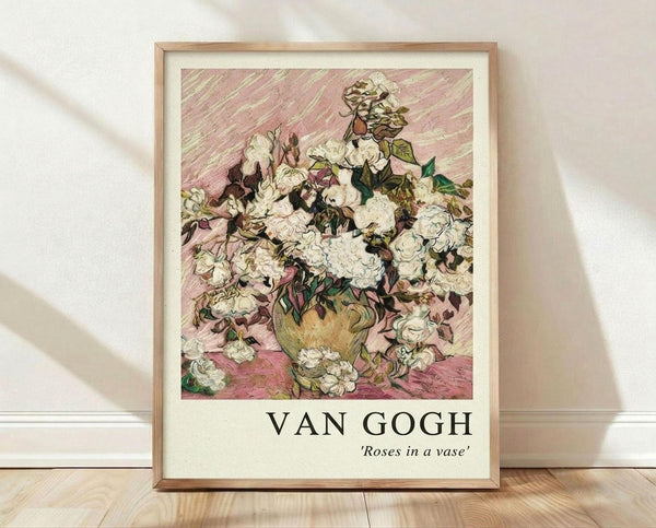May include: Framed art print of Van Gogh's white roses in a yellow vase against pink diagonal brushstroke background, displayed in light wood frame leaning against white wall on wooden floor with soft natural lighting and fabric shadows