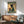 May include: Japanese-style poster featuring black cat in traditional green floral kimono holding red cup, with text "More Espresso Less Depresso" in green banner, displayed in wood frame above mid-century modern wooden credenza with white lamp, next to teal upholstered chair with wooden arms in bright living room with white walls and natural lighting