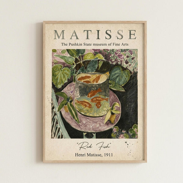 May include: Framed art print on cream-colored wall showing Matisse's colorful still life painting of red fish in a glass fishbowl surrounded by lush green foliage and purple fabric. The print features museum-style text layout with the artist's name at top and artwork title and date at bottom. Natural wood frame complements the vintage aesthetic of this Fauvism-style artwork with bold colors and expressive brushstrokes.