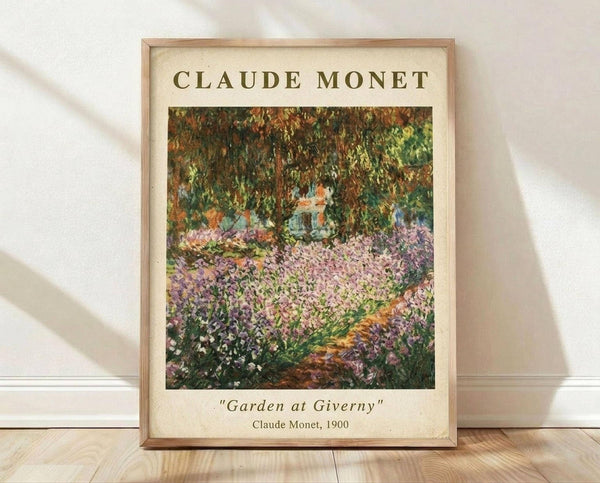 May include: Framed art print of Claude Monet's impressionist garden painting featuring vibrant purple and pink flowers in foreground with lush green trees overhead. Light wooden frame on cream matting displays the colorful Giverny garden scene with soft, painterly brushstrokes typical of Monet's style. Print sits on light wooden floor against white textured wall with natural lighting creating gentle shadows.