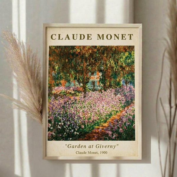 May include: Framed art print of Claude Monet's impressionist garden painting featuring vibrant pink and purple flowers in foreground with lush green trees overhead. Light wood frame with cream matting displays the colorful garden scene. Dried pampas grass visible to left side against soft beige curtains and white window light in minimalist room setting.