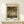 May include: Framed poster print of Claude Monet's impressionist garden painting featuring vibrant purple irises in foreground, lush green foliage and trees overhead, displayed on light wooden console table beside small white wrapped gift with evergreen sprig against cream wall