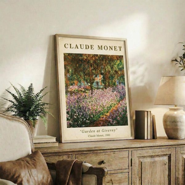 May include: Framed reproduction of Monet's garden painting featuring vibrant purple flowers and lush green foliage, displayed on rustic wooden sideboard alongside fern plant, ceramic vases, and books in neutral-toned living room with beige walls and upholstered furniture