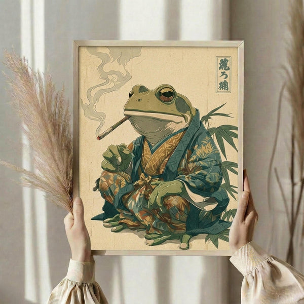 May include: Person in cream ruffled sleeves holding framed artwork showing anthropomorphic frog in traditional Japanese kimono smoking a pipe with steam wisps, surrounded by green foliage. Art features muted green and tan colors in vintage Japanese woodblock print style with characters in upper corner. Dried pampas grass visible to left against neutral background with soft natural lighting.