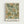 Vintage botanical wallpaper pattern featuring intricate green foliage, orange and coral flowers, and yellow leaves on a sage green background. The decorative design is displayed in a light wooden frame against a white wall, with text below reading "Morris & Company, 1866" and "William Morris" in black lettering.