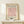 May include: Framed art print displaying minimalist line drawing of flamingo in pink on cream background, positioned on light wooden shelf next to small wrapped gift with twine and greenery sprig against neutral wall