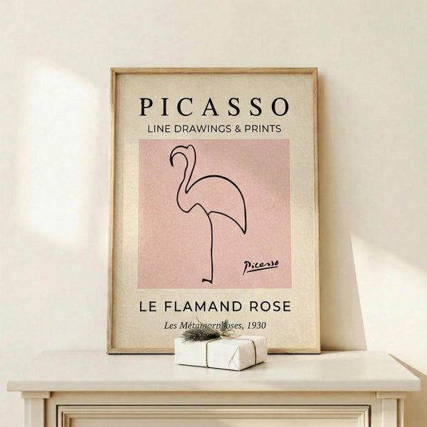 May include: Framed art print displaying minimalist line drawing of flamingo in pink on cream background, positioned on light wooden shelf next to small wrapped gift with twine and greenery sprig against neutral wall
