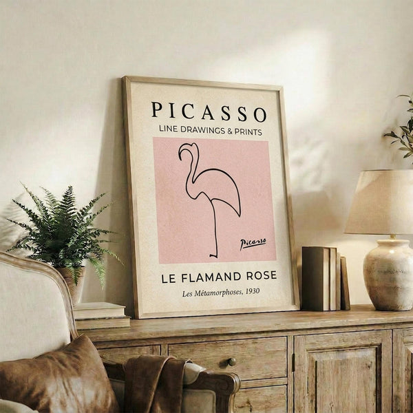 May include: Framed art print featuring minimalist line drawing of pink flamingo on rose background, displayed on rustic wooden console with books, ceramic vases, and fern plant. Cream matting in light wood frame against neutral wall in modern living room setting.