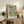 May include: Framed botanical print with green sage background featuring detailed leaves, orange berries, and cream flowers in William Morris Arts and Crafts style. Light wood frame sits on rustic wooden sideboard next to fern plant, ceramic vase, and books in neutral-toned living room with beige chair and cream walls.