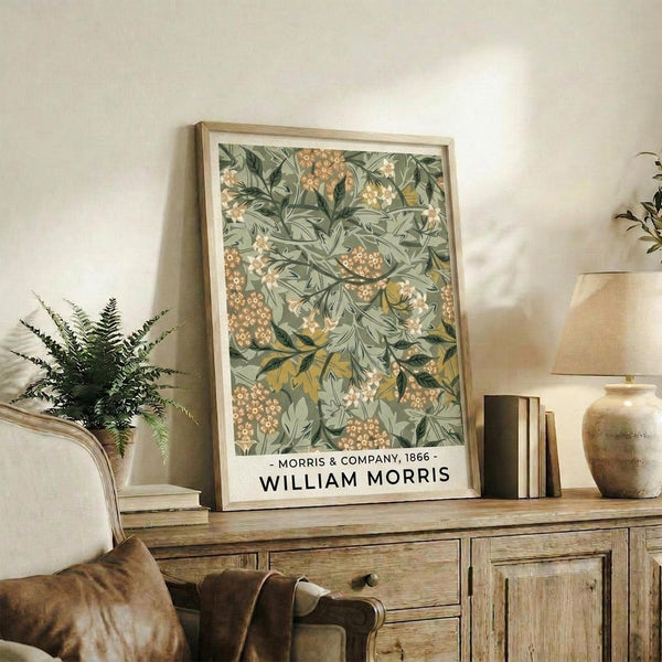 May include: Framed botanical print with green sage background featuring detailed leaves, orange berries, and cream flowers in William Morris Arts and Crafts style. Light wood frame sits on rustic wooden sideboard next to fern plant, ceramic vase, and books in neutral-toned living room with beige chair and cream walls.