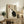May include: Framed poster with beige background featuring black and white cats in yin yang formation, red and black Japanese characters above. Wooden frame rests on rustic wood sideboard beside fern plant, books, ceramic vases. Cream chair with brown throw blanket visible in cozy living room setting with white walls.