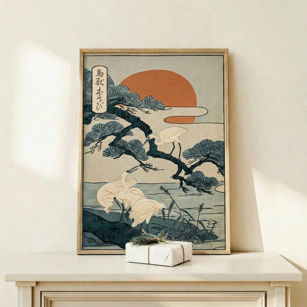 May include: Japanese woodblock print artwork in light wood frame showing white cranes near pine tree with orange sun and blue-green foliage, displayed on light wood console table with small white wrapped gift, against cream wall in minimalist room setting.