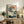 May include: Japanese woodblock print featuring white cranes near water with pine tree branches, orange sun, and Japanese text, displayed in light wood frame on rustic wooden sideboard alongside fern plant, ceramic vase, and books in neutral-toned living room setting.