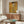May include: Gustav Klimt's golden portrait of Adele Bloch-Bauer displayed as a framed print above a mid-century modern walnut credenza in a minimalist living room. The artwork features intricate gold leaf patterns and geometric designs surrounding an elegant woman in ornate dress. Room includes white curved chair, oval glass coffee table, brass floor lamp, and white table lamp on cream walls.