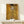 May include: Ornate golden portrait painting in light wood frame displayed on white wooden console table with small wrapped gift box. The artwork features a woman in elaborate patterned dress surrounded by intricate geometric designs and swirling motifs in rich golds, yellows and earth tones. The decorative Art Nouveau style shows detailed ornamental elements throughout the composition against a luxurious golden background.
