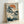 May include: Framed Japanese woodblock print showing white cranes near water with a gnarled pine tree, orange sun, and Japanese text in upper left corner. The artwork features traditional ukiyo-e style with blue-green tones and cream background, displayed in light wood frame leaning against white wall.