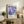 A framed poster of Yayoi Kusama's artwork hangs on a wall in a living room, surrounded by various decorative items such as a potted plant, books, and a lamp.